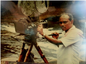 K.S. Gopalakrishnan by a large camera. 